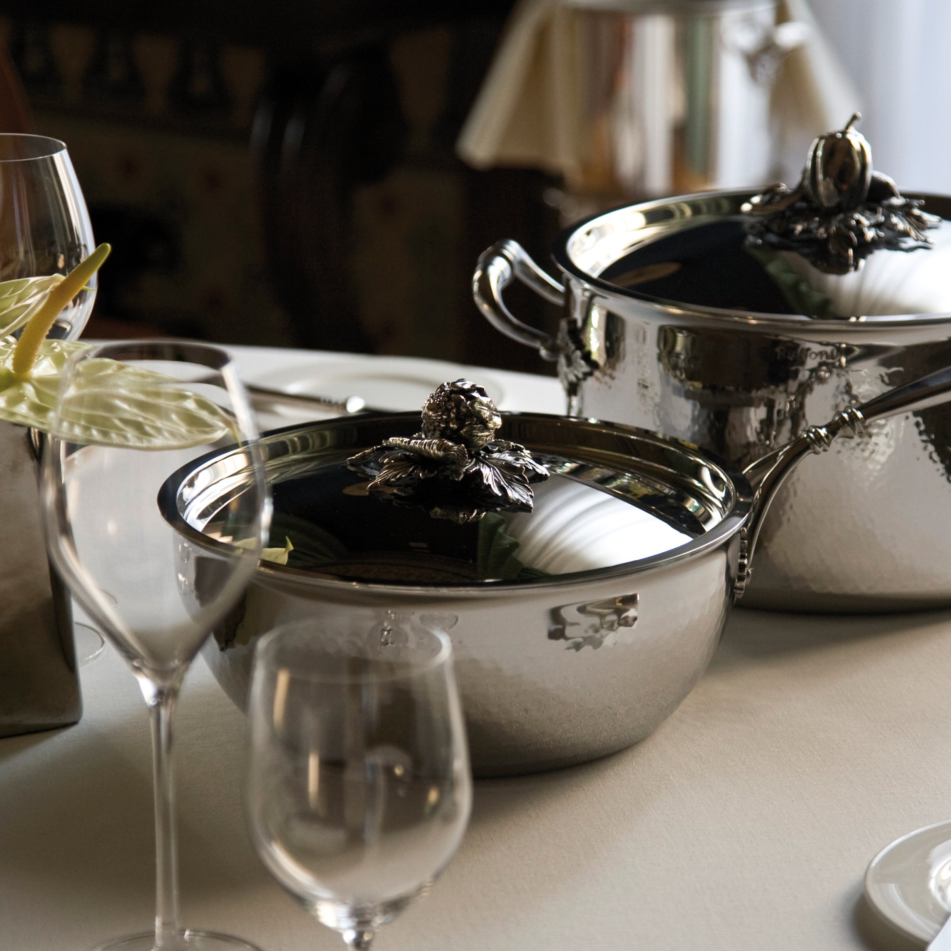 Opus Prima hammered clad stainless steel chef pan and stockpot with decorated silver-plated lid knob finial from Ruffoni on a classic tablesetting