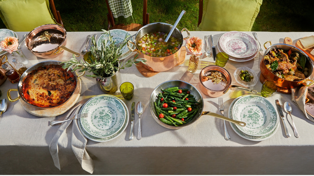 Olivia Cupra collection on a beige linen tablecloth with green plates and glasses in the Italian countryside on a summer day