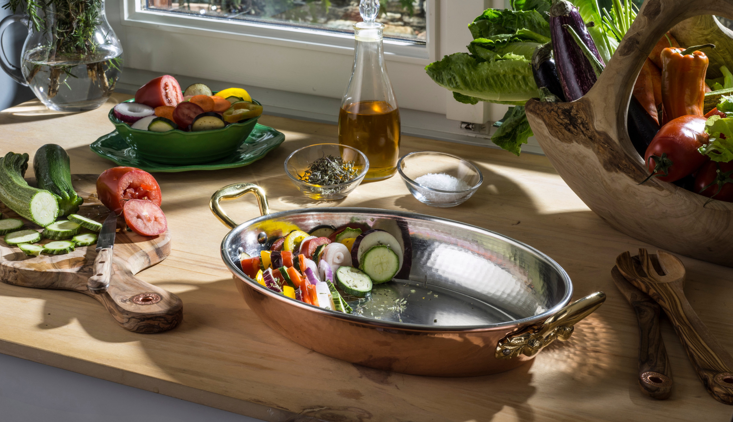 Ruffoni copper roasting pan with vegetables on a sunlit kitchen counter.