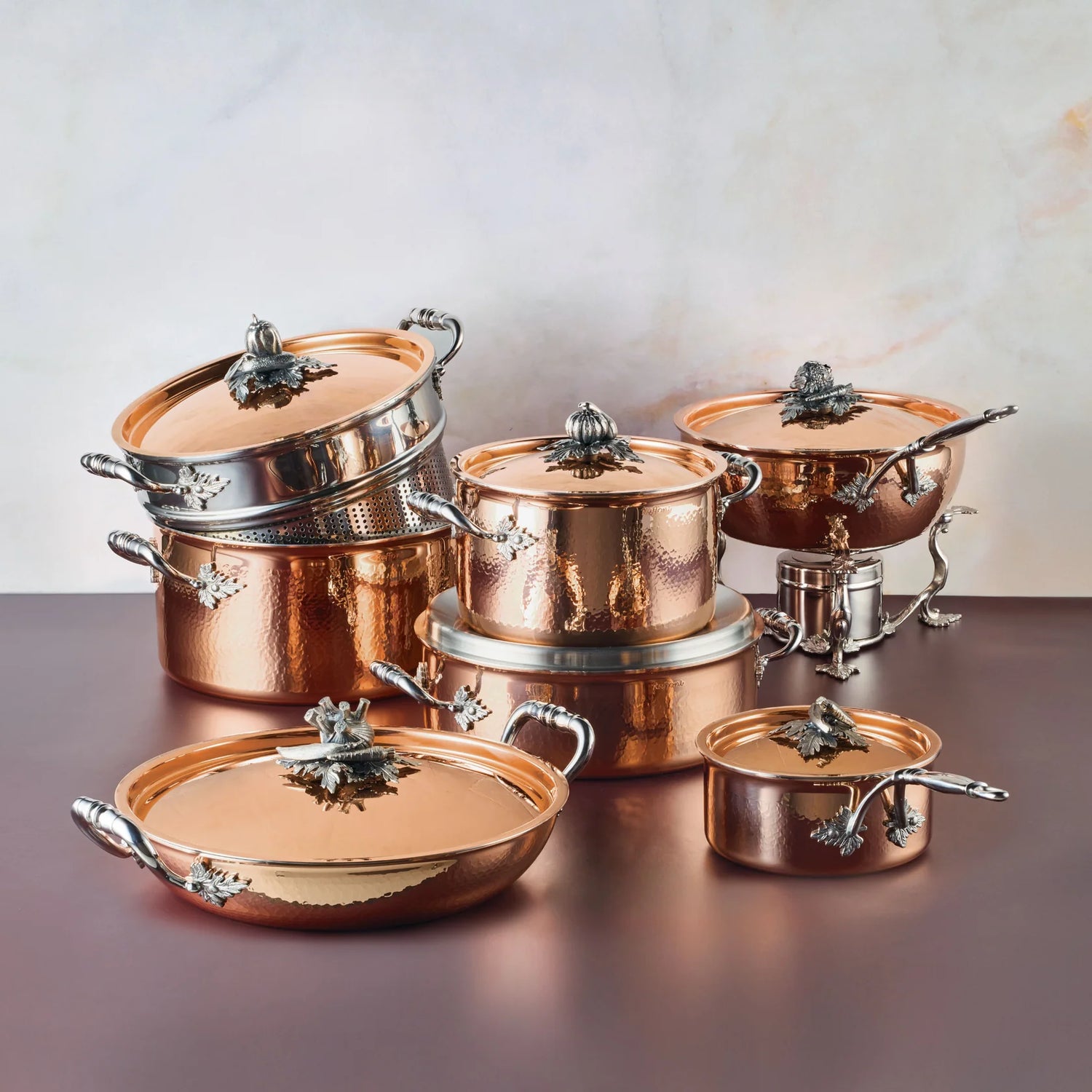 Set of copper cookware with silver handles on a reflective surface.