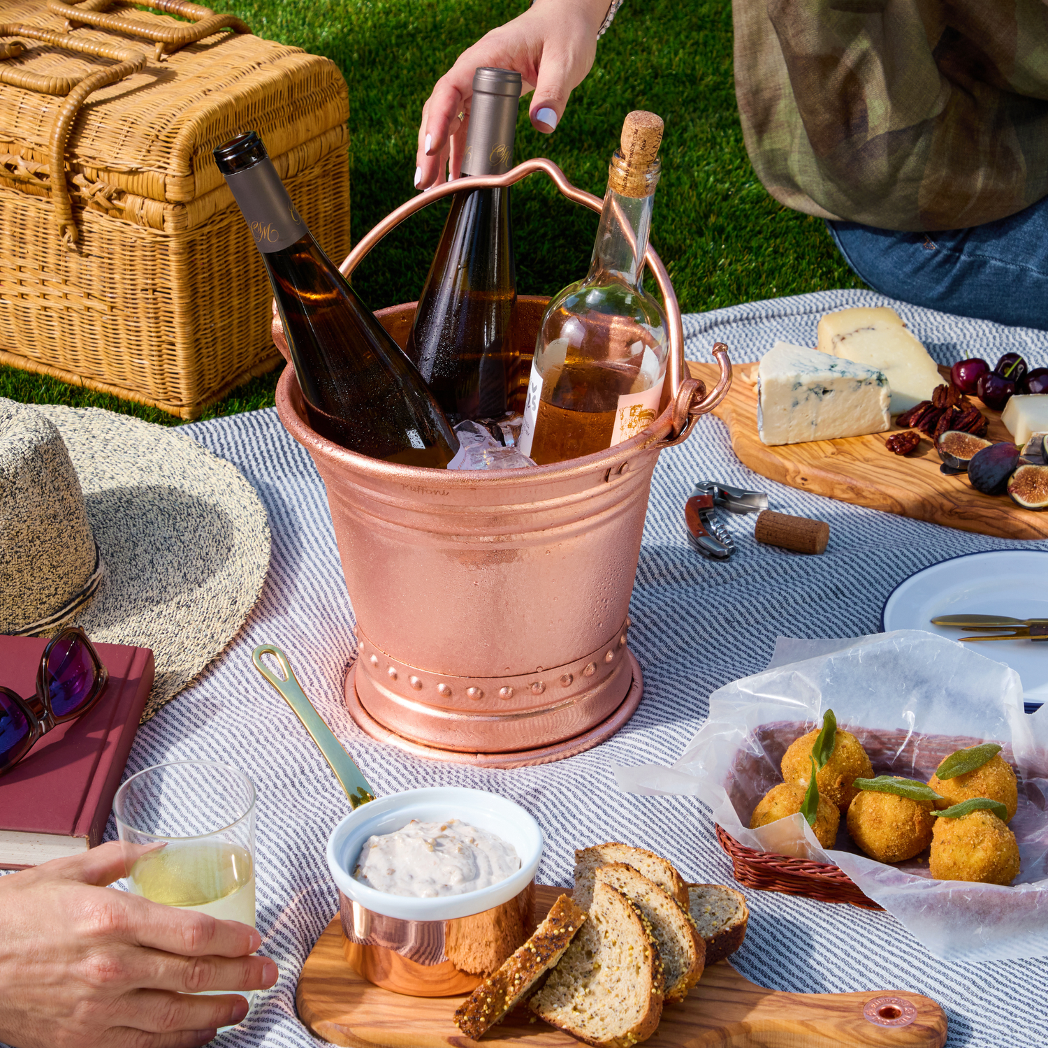 Picnic setup with wine, cheese, and snacks on a blanket outdoors.