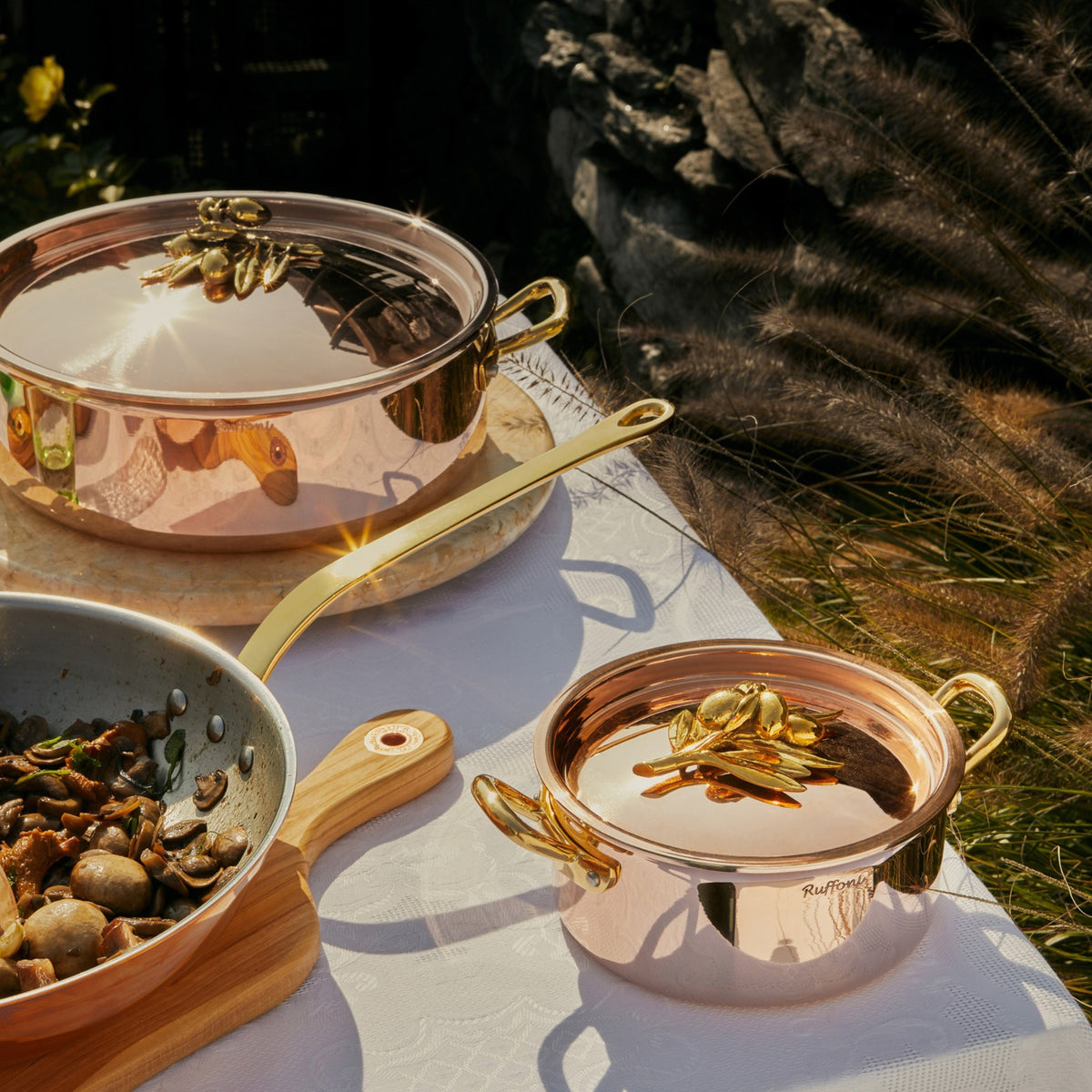 Olivia Cupra collection on a beige linen tablecloth with green plates and glasses in the Italian countryside on a summer day