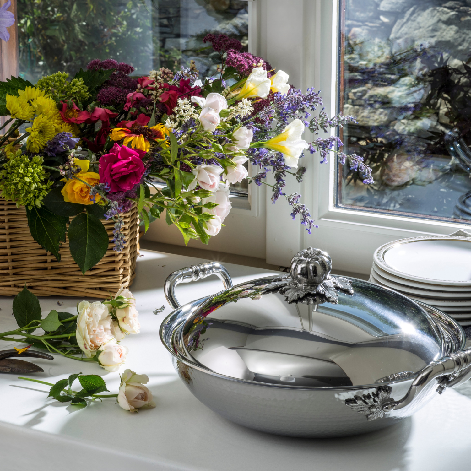 Silver casserole dish with floral arrangement on a windowsill