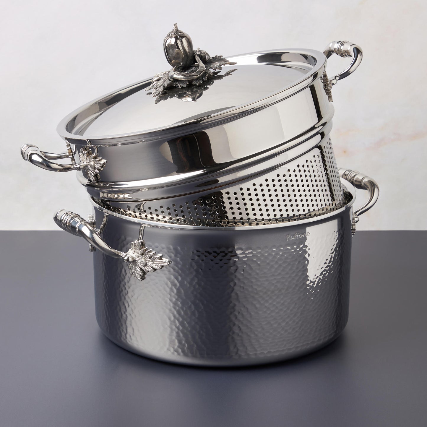 Opus Prima hammered clad stainless steel stockpot with decorated silver-plated lid knob finial from Ruffoni photographed with the matching pasta insert